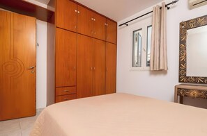 A bedroom with a bed, wooden wardrobe, a window with curtains, and a mirror with a decorative frame.