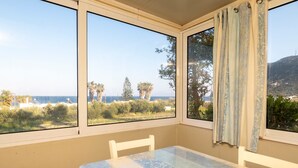 Ein Zimmer mit Tisch und zwei Fenstern, das Blick auf Strand und Berge bietet.