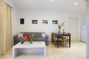 A living room with a sofa, a coffee table with flowers, a dining table with chairs, and a door. - Holiday Home 'Two Bedroom' with Sea View, Wi-Fi and Air Conditioning (Kos)