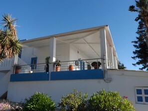A building with a balcony, potted plants, and a clear blue sky.