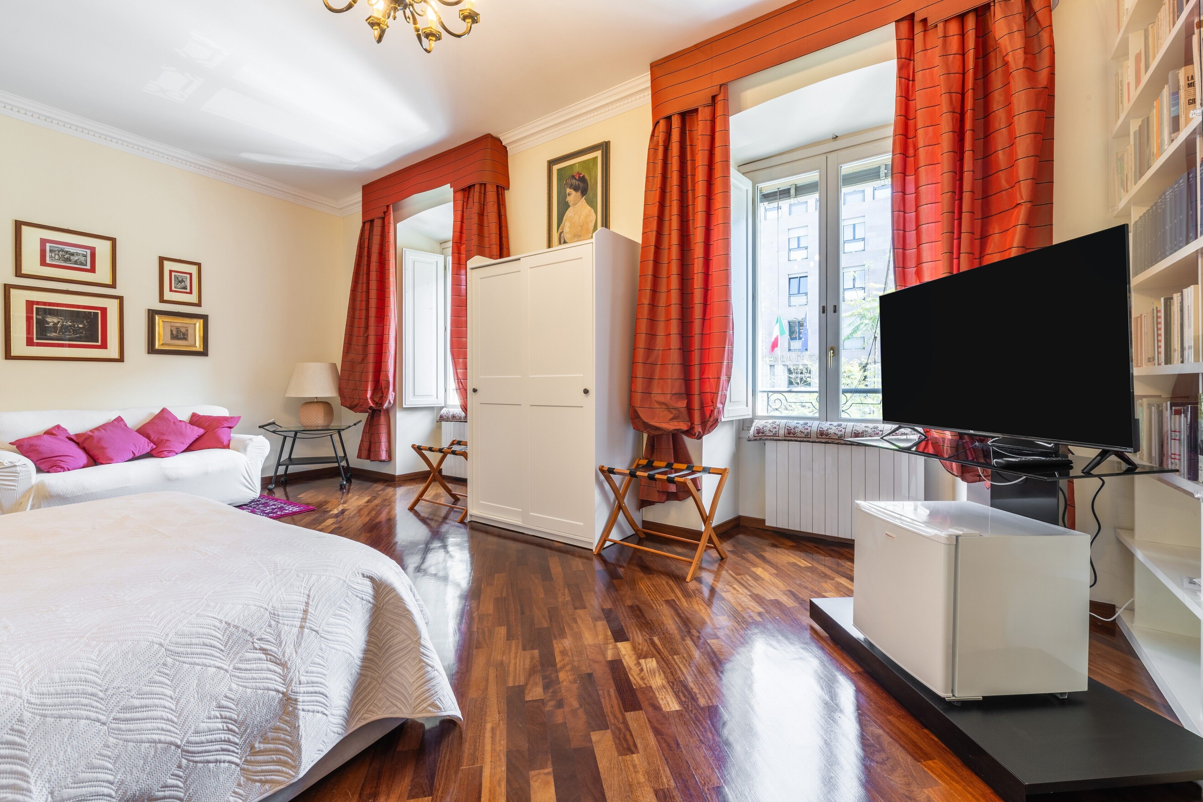 A bedroom with a bed, a wardrobe, a television, and a window with curtains.