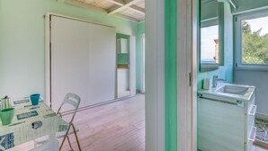 A room with a table, chairs, a white door, a window with a view, and a bathroom with a sink and mirror.