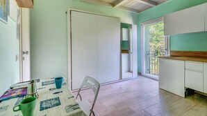 A room with a wooden ceiling, a white door, a table with a chair, and a window with a view of trees.