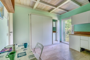 A room with a wooden ceiling, a white door, a table with a chair, and a window with a view of trees.