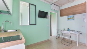 A room with a kitchen area, a desk with a chair, a television, and a map on the wall.