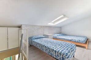 Een studentenkamer met twee bedden, een kledingkast, een bureau en een dakraam.