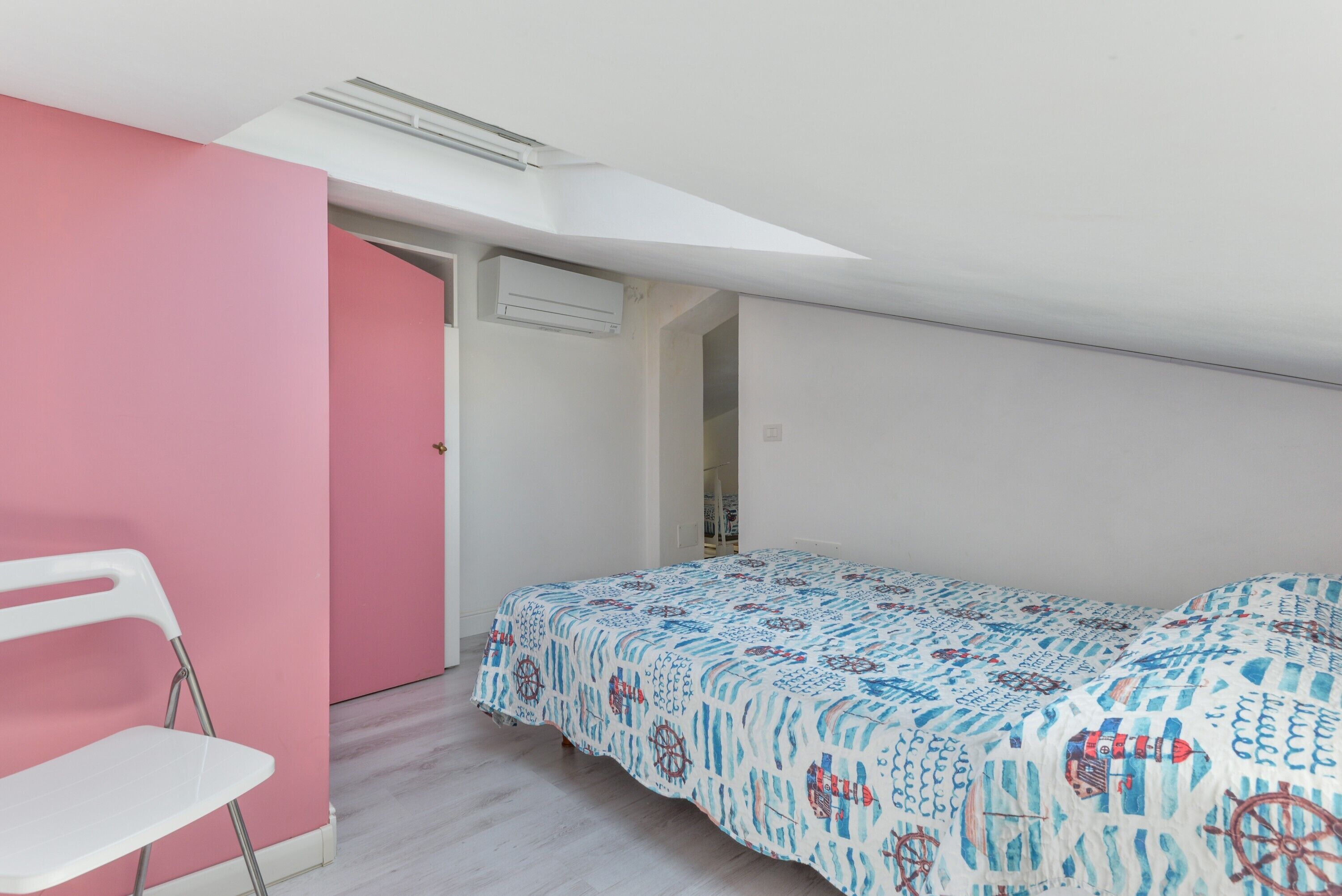 A bedroom with a bed, a white chair, a pink wall, and a skylight.