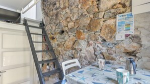 Un muro de piedra, una puerta blanca, una mesa con mantel, una silla, una escalera, un hervidor y una taza.