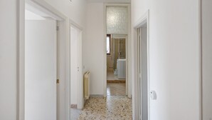 Un pasillo con paredes blancas, un radiador y suelo de baldosas que conduce a un baño con ducha y retrete.