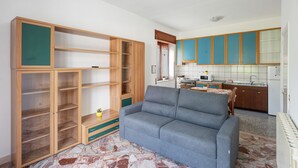 Una sala de estar con un sofá gris, armarios de madera y una cocina con armarios azules y salpicadero de azulejos.