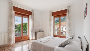 Un dormitorio con cama, cortinas, cómoda y vistas a edificios y árboles.