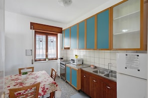 A compact kitchen with a dining table, a microwave, a refrigerator, and wooden cabinets.