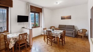 A dining area with a table and chairs, a sofa, a television, and a window with a view.