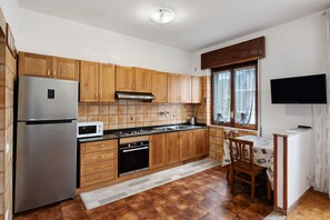 A kitchen with wooden cabinets, a stainless steel refrigerator, a microwave, a stove, and a dining area with a table and chairs.