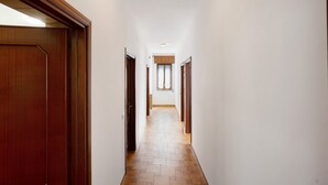 A narrow hallway with wooden doors on both sides, leading to a room with a window.