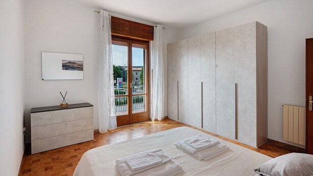 A bedroom with a bed, a dresser, a wardrobe, and a window with curtains.