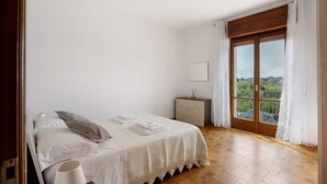 A bedroom with a bed, a bedside table, a nightstand, and a view through a large window.