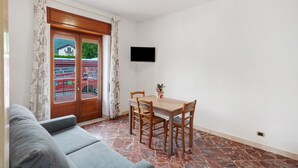 A room with a dining table, chairs, a TV mounted on the wall, and a sofa.