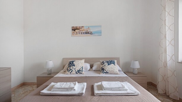 A hotel room with a bed, two nightstands, a painting, and a view of the sea.
