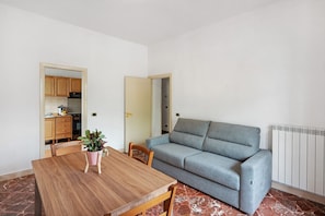 Ein Wohnzimmer mit einer Couch, einem Esstisch und einer durch eine offene Tür einsehbarer Küche.