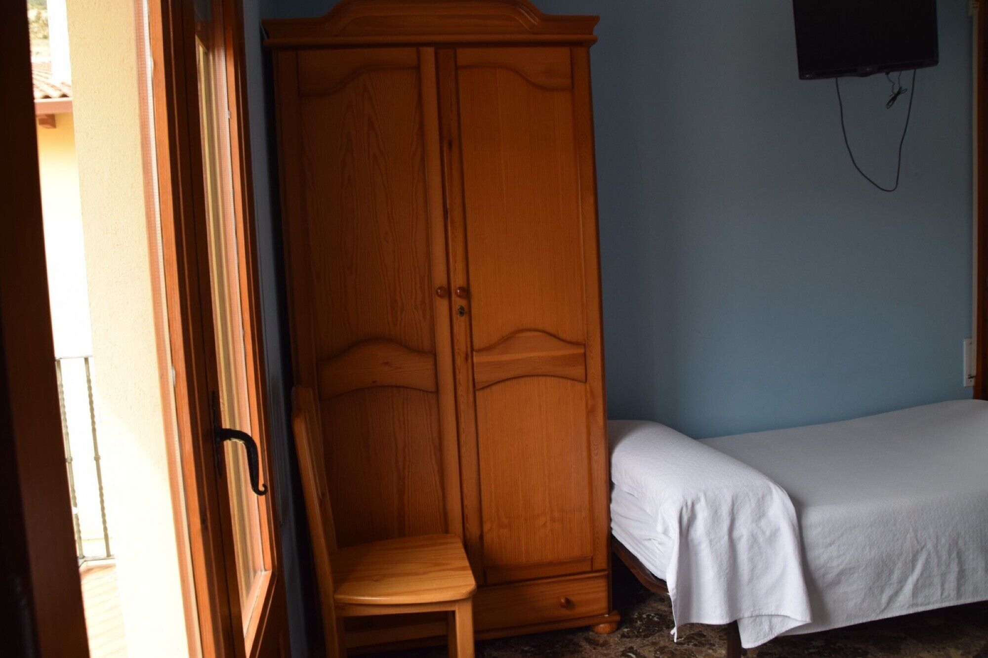 Un dormitorio con un armario de madera, una cama individual y una silla.