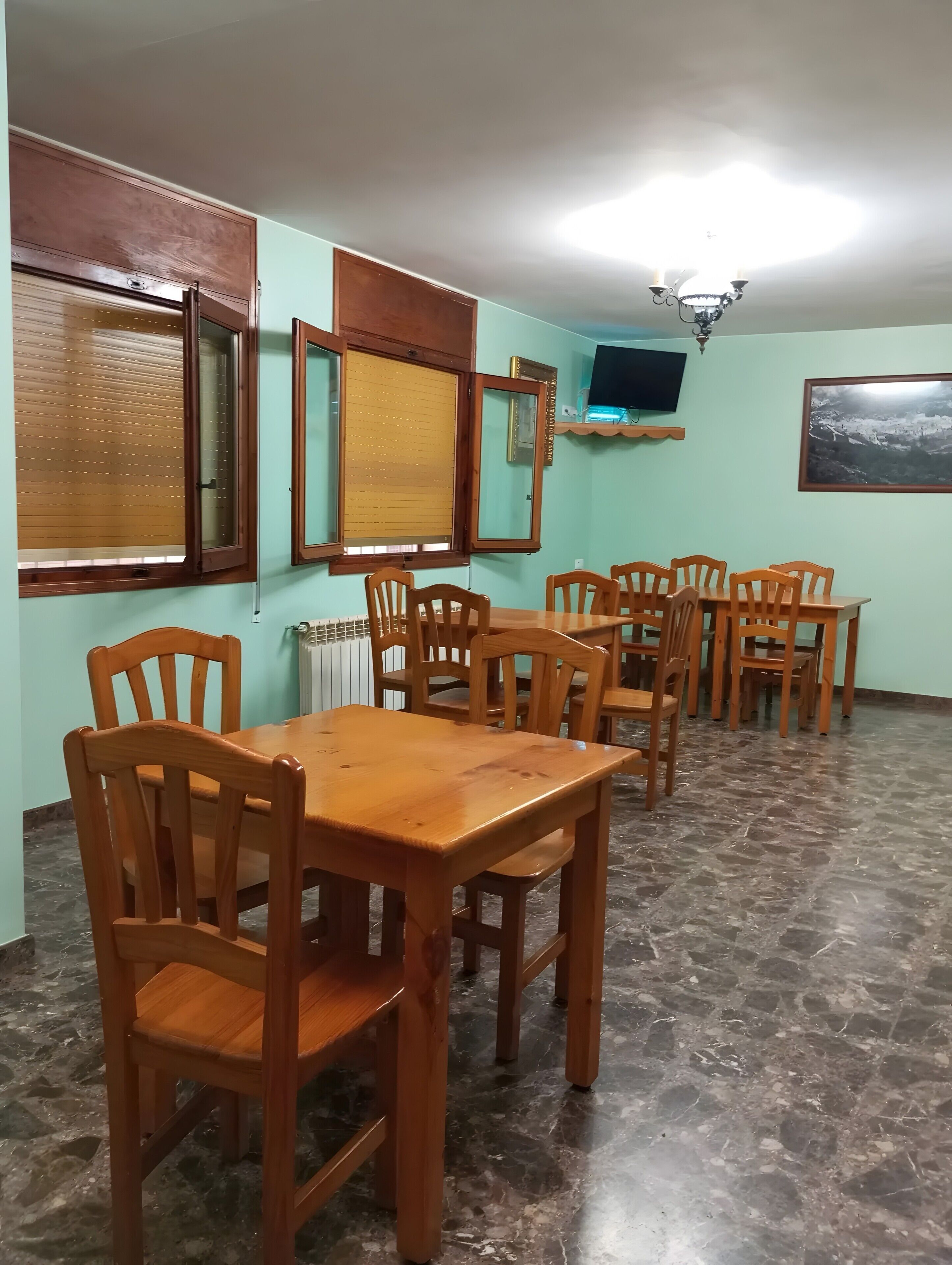 Un comedor con mesa y sillas de madera, un televisor en la pared y una ventana con persianas.