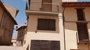 A two-story building with a balcony, a garage door, and a clear sky with clouds. - Room 'Twin Con Balcón' with Balcony and Wi-Fi (Villarluengo)