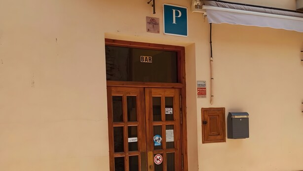 A building with a wooden door labeled 'BAR,' a 'P' parking sign, and a security camera. - Room 'Twin Con Balcón' with Balcony and Wi-Fi (Villarluengo)