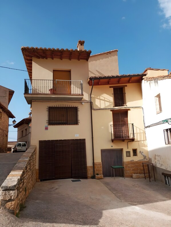 A two-story building with a tiled roof, a balcony, a garage, and a small garden area.