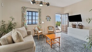 Una sala de estar con sofá, sillas, mesa de centro, televisor y balcón con plantas.