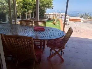 Un espace patio avec une table ronde, des chaises en bois et une vue sur la mer.