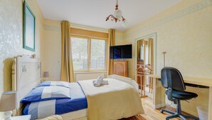 A bedroom with a bed, a desk, a chair, a TV, and a window.