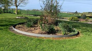 A well-maintained garden with a circular flower bed, a tree, and a grassy lawn.