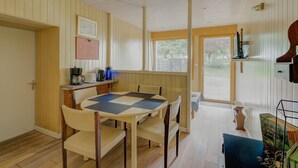 A dining area with a checkered table, chairs, a coffee machine, and a view through a glass door.