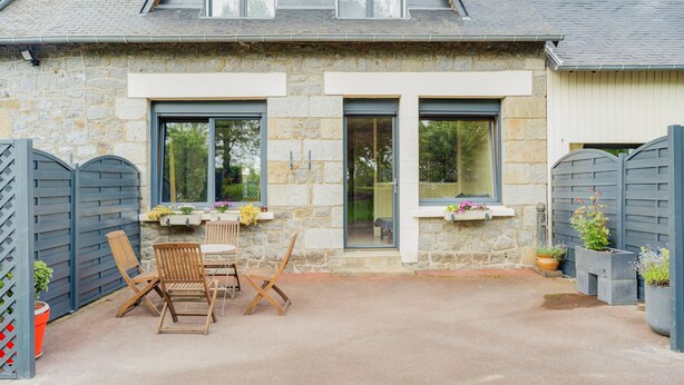 A stone building with a patio, wooden chairs, and potted plants.