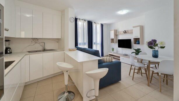 Una cocina moderna con armarios blancos, un lavamanos integrado y una barra con taburetes.