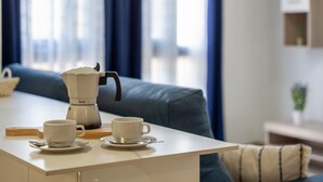 Una cocina moderna con una cafetera, dos tazas sobre una mesa y un sofá al fondo.