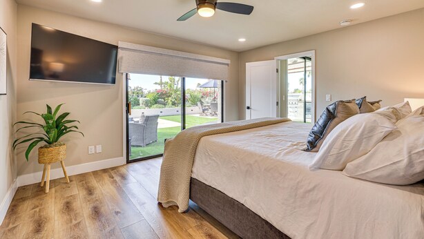 A bedroom with a large bed, a ceiling fan, a TV mounted on the wall, and a sliding glass door leading to a patio. - Private Pool + Putting Green: Sunny Scottsdale Gem (Scottsdale)
