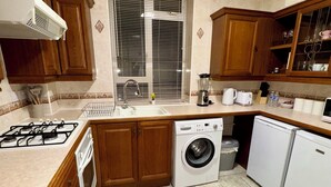 A compact kitchen with wooden cabinets, a gas stove, a washing machine, and a refrigerator. - Vauxhall, river Thames, Big Ben Retreat, Central London family Stay (London)