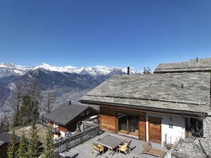 Een chalet met stenen dak, houten gevel en een balkon met uitzicht op een besneeuwd berglandschap.