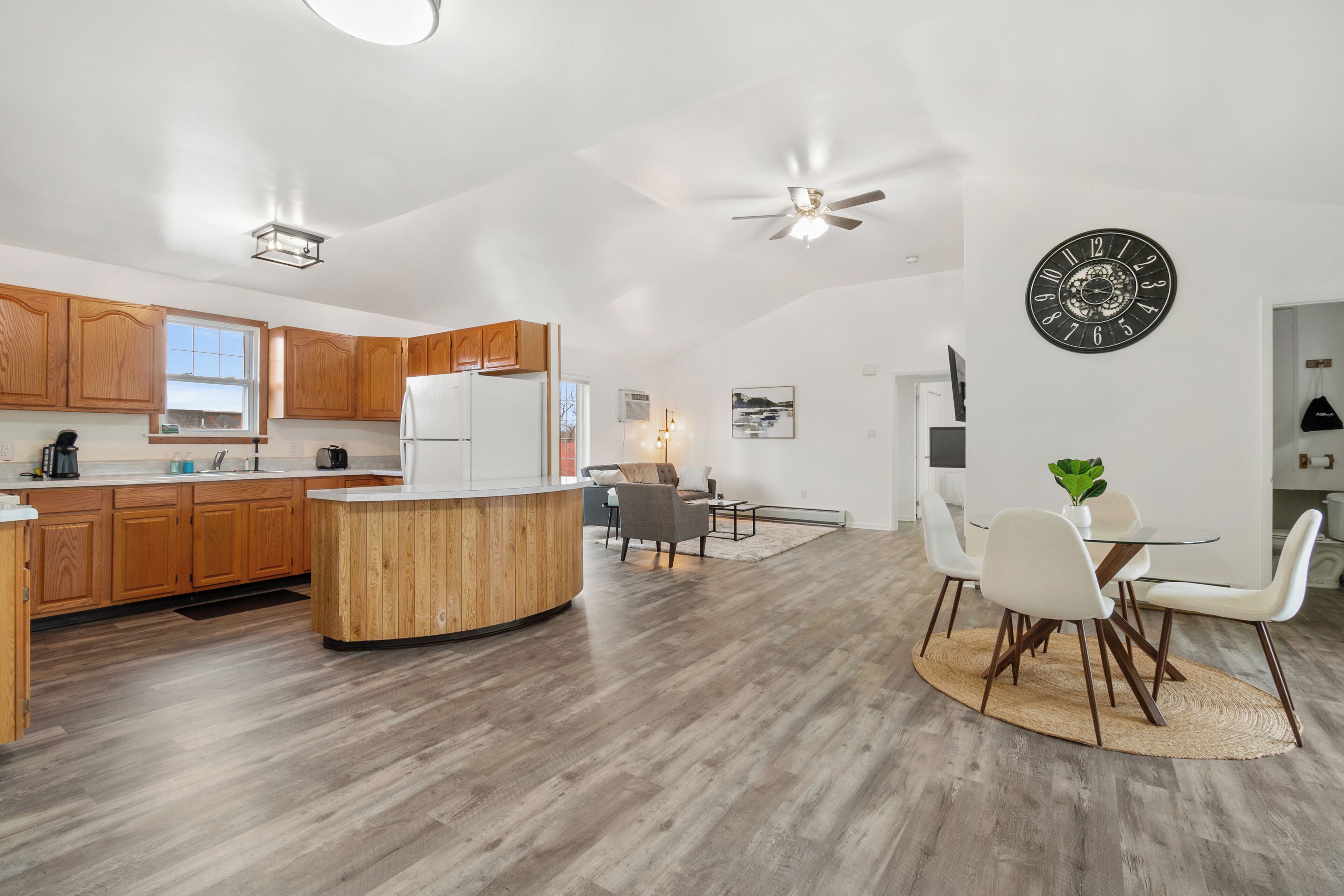 Eine moderne Küche mit Holzschränken, einer zentralen Kochinsel und einem Essbereich mit weißen Stühlen und einem Tisch.