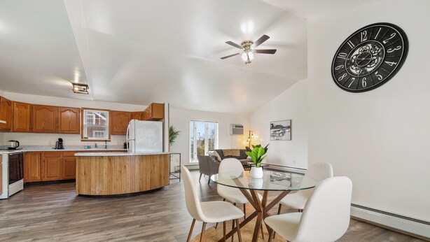 A modern kitchen with wooden cabinets, a central island, and a dining area with a glass table and white chairs.