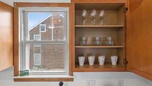 A kitchen with a window, wooden cabinets, and shelves with glassware and cups.