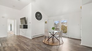 A spacious room with a dining table and chairs, a mounted TV, and a large window with a view of trees.