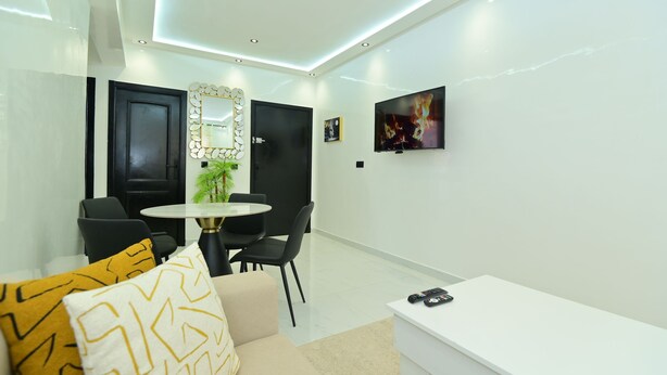 A modern living room with a sofa, a dining table, and chairs. There is a TV mounted on the wall and an air conditioning unit above it. - 12 min to Majorelle 2BR Oasis AC & Free Parking (Marrakesh)