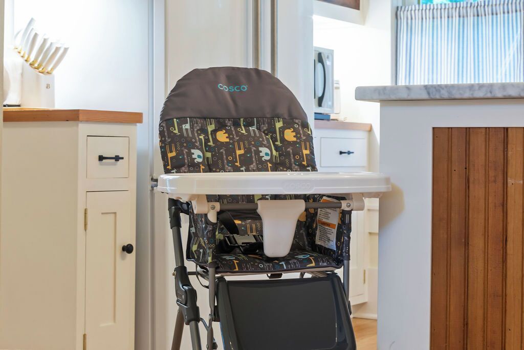A baby stroller with a patterned seat cover and a canopy, placed on a white shelf in a room with a wooden door and a white cabinet.