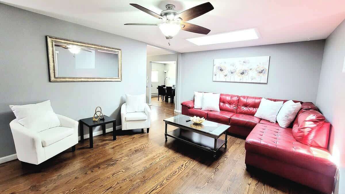 A living room with a red leather sofa, white armchairs, a coffee table, and a ceiling fan.