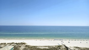 A beach with a clear sky, sandy shore, and a wooden walkway leading to the water.