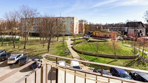 A parking area with multiple cars, a grassy park with trees, and buildings in the background.