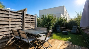 An outdoor patio with a wooden table and chairs, surrounded by a wooden fence and greenery.